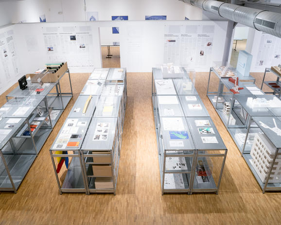 vue d'exposition avec 4 grandes tables où des maquettes et images sont disposées